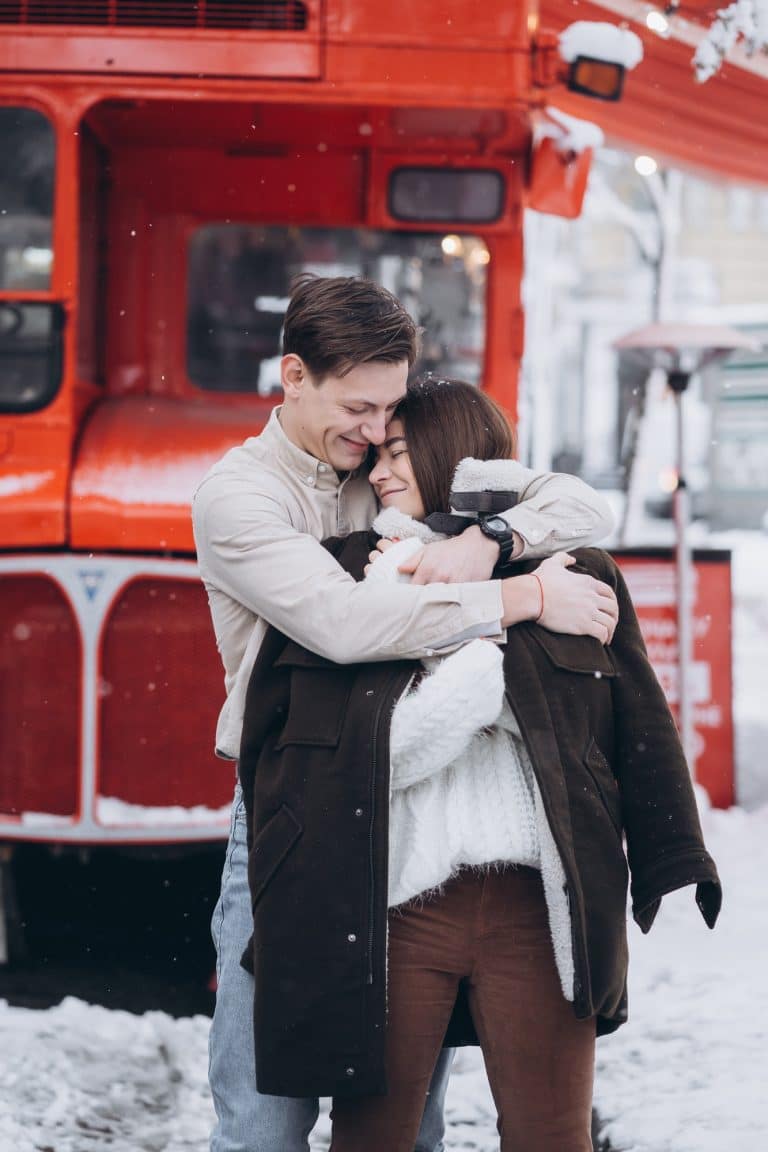 young guy warms his beautiful girl with jacket on a snowy street